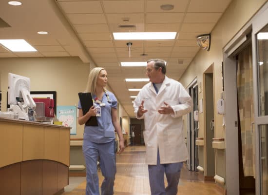 A nurse and Randy Carter, MD talking as they walk down a hospital hallway.