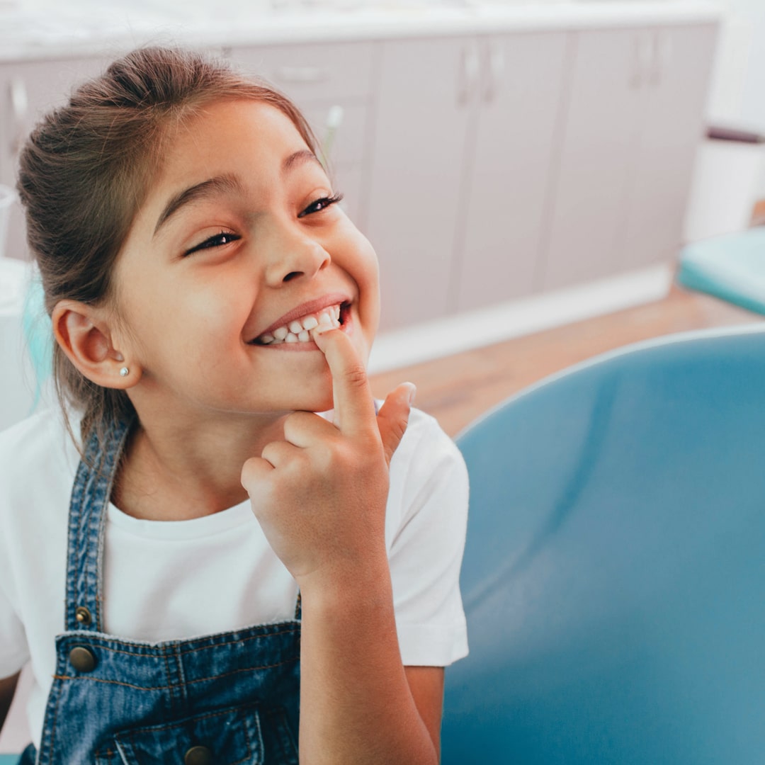 Smiling girl pointing toward her teeth in a dentists office - Foundation photo.